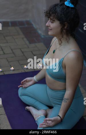 In einer Hochwinkel-Nahaufnahme sitzt eine junge Frau anmutig in einer Lotusposition mit einem ruhigen Ausdruck Stockfoto