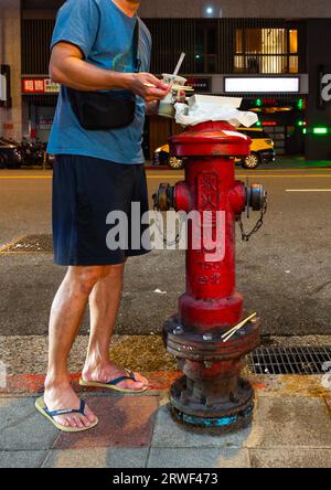 Mann, der sein Essen auf einen Feuerhydranten im Nanjichang Nachtmarkt, Bezirk Zhongzheng, Taipei, Taiwan, stellt Stockfoto
