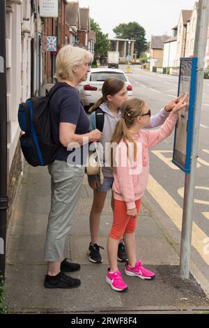 Junge Mädchen mit Großmutter, die an einer Bushaltestelle stehen und versuchen, den Zeitplan oder den Zeitplan zu ermitteln, öffentliche Verkehrsmittel Stockfoto