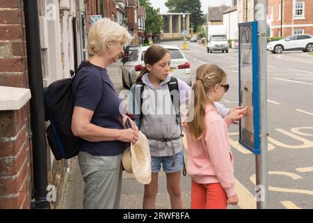 Junge Mädchen mit Großmutter, die an einer Bushaltestelle stehen und versuchen, den Zeitplan oder den Zeitplan zu ermitteln, öffentliche Verkehrsmittel Stockfoto