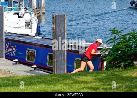 Eine attraktive Frau mittleren Alters in Shorts, Hut und rotem Oberteil, die ein schmales Boot an der Themse im Shepperton Surrey England anlegt Stockfoto