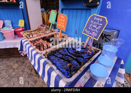 Eine lebendige, farbenfrohe Szene im Chefchaouen Souk mit dekorativer marokkanischer schwarzer Seife in Tabletts auf einem blau-weiß gestreiften Tuch und anderen Souvenirs zum Verkauf Stockfoto