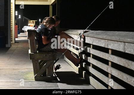 Zwei junge Frauen fischen nach Einbruch der Dunkelheit am Jennette's Pier in Nags Head. Stockfoto