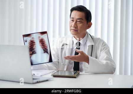 Arzt, der Röntgenthorax zeigt, wenn er mit dem Patienten in einer Online-Besprechung spricht Stockfoto