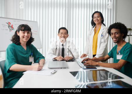 Glückliches medizinisches Team, das am großen Tisch in der Klinik sitzt Stockfoto