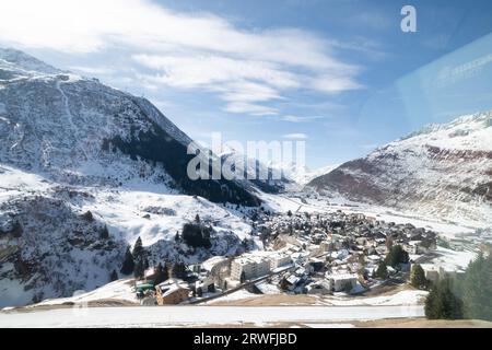Blick durch das Fenster auf den Glacier Express, Schweiz, mit Bergen und einer Stadt im Tal. Stockfoto