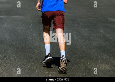 Rückansicht männlicher Läufer, der auf dunklem Asphalt bergauf läuft, Sommermarathonrennen Stockfoto
