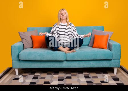 Foto einer ruhigen, friedlichen Rentnerin, die bequem im Diwan sitzt, im flachen, isolierten, hellen Farbhintergrund Stockfoto