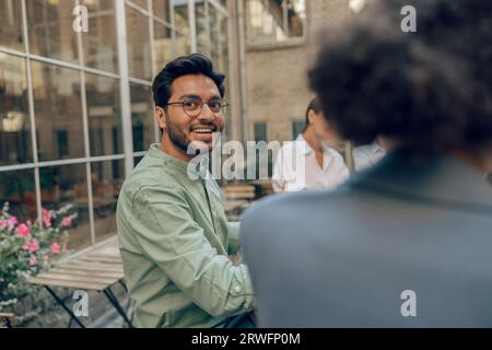 Lächelnder männlicher Manager, der die Kamera anschaut, während er mit Kollegen auf der Coworking-Terrasse sitzt Stockfoto