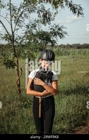 Porträt eines Mädchens - ein Jockey in einem Helm und ein weißes T-Shirt, das ein schwarzes Pferd umarmt - ein Spielzeug auf einem Stock, schaut auf das Spielzeug. Hobbyhorsing. Stockfoto