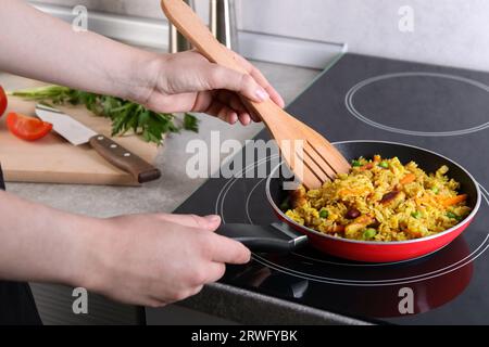 Frau frittiert Reis mit Fleisch und Gemüse auf Induktionskochfeld in der Küche, Nahaufnahme Stockfoto