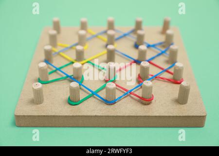 Geobord aus Holz mit Gummibändern auf grünem Hintergrund, Nahaufnahme. Lernspielzeug für die Entwicklung motorischer Fähigkeiten Stockfoto