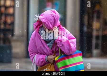 Frau, die an einem regnerischen Tag Kapuze über Gesicht hält Preston, Lancashire. Wetter in Großbritannien 19. September 2023. Geschäfte, Shopper, die an einem windigen Tag mit starken Duschen in Preston einkaufen. Es bleibt windig, mit Orkanen im Westen. Es wird heute Nachmittag mit heftigen und anhaltenden Regenfällen gerechnet. Stockfoto