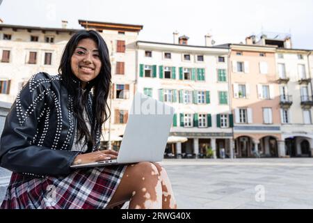 Ein junges Latina-Mädchen mit Vitiligo benutzt ihren Laptop, während sie im Stadtzentrum sitzt Stockfoto