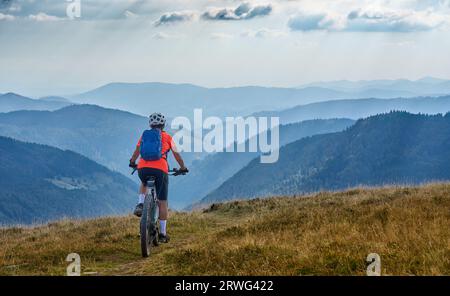 Nette Seniorin auf ihrem Elektro-Mountainbike auf dem Feldberg mit atemberaubendem Blick über die Berge und Täler des Schwarzwaldes Stockfoto