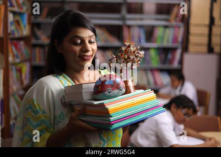 Indische Lehrerin hält ein Bündel Bücher in der Hand, steht in der Bibliothek, studiert Druck, erzieherische Kraft. Stockfoto