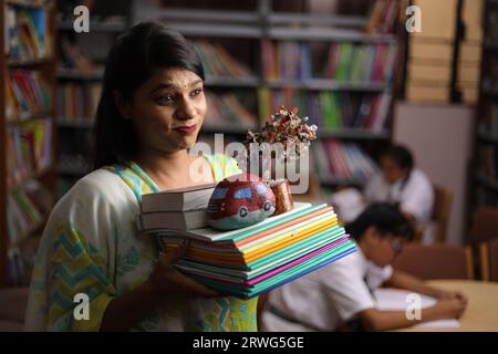 Indische Lehrerin hält ein Bündel Bücher in der Hand, steht in der Bibliothek, studiert Druck, erzieherische Kraft. Stockfoto