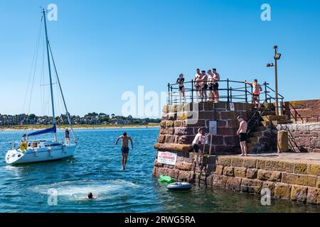 Kinder, die bei heißem Sommerwetter vom Kai ins Meer springen, North Berwick Harbour, East Lothian, Schottland, Großbritannien Stockfoto