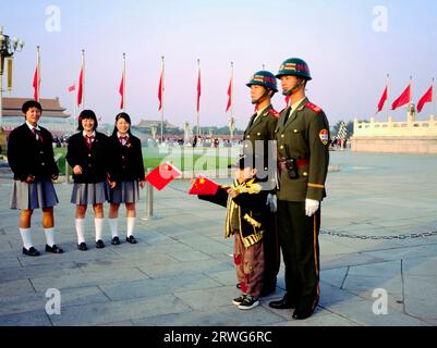 PEKING, CHINA - 19. JULI 2018: Chinesische Soldaten im Dienst auf dem Tian an Men Square posieren mit einem Kind mit chinesischen Fahnen für ein Foto, während die Schüler W sind Stockfoto