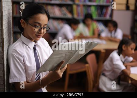 Kluger Schüler, der sich an die Wand lehnt, ein Buch in der Hand liest, konzentriert, Nerd, Leser, in der Bibliothek. Stockfoto