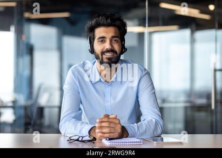 Porträt eines jungen indischen Lehrers in einem Headset, der vor der Kamera im Büro sitzt und online spricht. Stockfoto