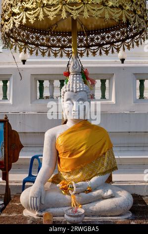 Eine sitzende weiße Buddha-Figur auf dem Gelände von Wat Pichaiyat, Thonburi, Bangkok, Thailand, bedeckt von einem zeremoniellen Regenschirm Stockfoto