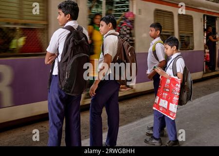 Schuljungen, die am Chhatrapati Shivaji Maharaj Terminus in Mumbai, Indien, dem belebtesten Bahnhof der Stadt, auf einen ankommenden Vorortzug warten Stockfoto