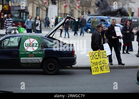 Die Teilnehmer treffen sich mit Plakaten während eines Protestes gegen die Erweiterung der Londoner Umweltzone um den Trafalgar Square in London. Stockfoto