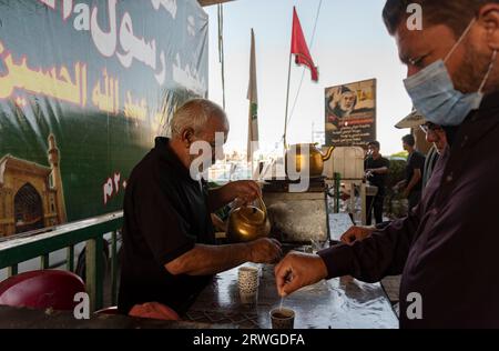 Najaf, Irak. September 2023. Ein irakischer Mann verteilt Tee unter schiitisch-muslimischen Pilgern, die von Najaf in die Schreinerstadt Karbala marschieren. Jedes Jahr pilgern Millionen schiitische Muslime und einige aus anderen Glaubensrichtungen zu Fuß von verschiedenen Städten im Irak und Iran in die heilige Stadt Karbala. Diese Pilgerfahrt erinnert an Imam Hussein, den Enkel des Propheten Mohammed, der 680 n. Chr. in einer Schlacht starb. Am 40. Tag der Trauer um Hussein, bekannt als Arbaeen, kommen Pilger in Karbala zusammen, um an seinem Heiligtum Tribut zu zollen. Auf dem Weg stellen Freiwillige Nahrung, Wasser und sie zur Verfügung Stockfoto