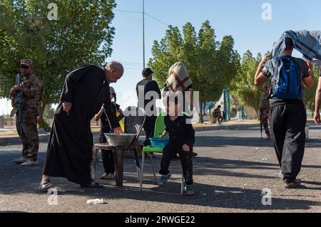 Najaf, Irak. September 2023. Irakische schiitische Kinder verteilen Wasser unter schiitisch-muslimischen Pilgern, die von Najaf in Richtung der Schreinerstadt Karbala marschieren. Jedes Jahr pilgern Millionen schiitische Muslime und einige aus anderen Glaubensrichtungen zu Fuß von verschiedenen Städten im Irak und Iran in die heilige Stadt Karbala. Diese Pilgerfahrt erinnert an Imam Hussein, den Enkel des Propheten Mohammed, der 680 n. Chr. in einer Schlacht starb. Am 40. Tag der Trauer um Hussein, bekannt als Arbaeen, kommen Pilger in Karbala zusammen, um an seinem Heiligtum Tribut zu zollen. Auf dem Weg stellen Freiwillige Nahrung, Wasser, und zur Verfügung Stockfoto