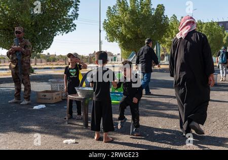 Najaf, Irak. September 2023. Irakische schiitische Kinder verteilen Wasser unter schiitisch-muslimischen Pilgern, die von Najaf in Richtung der Schreinerstadt Karbala marschieren. Jedes Jahr pilgern Millionen schiitische Muslime und einige aus anderen Glaubensrichtungen zu Fuß von verschiedenen Städten im Irak und Iran in die heilige Stadt Karbala. Diese Pilgerfahrt erinnert an Imam Hussein, den Enkel des Propheten Mohammed, der 680 n. Chr. in einer Schlacht starb. Am 40. Tag der Trauer um Hussein, bekannt als Arbaeen, kommen Pilger in Karbala zusammen, um an seinem Heiligtum Tribut zu zollen. Auf dem Weg stellen Freiwillige Nahrung, Wasser, und zur Verfügung Stockfoto