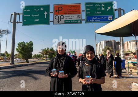 Najaf, Irak. September 2023. Irakische schiitische Mädchen verteilen Wasser unter schiitisch-muslimischen Pilgern, die von Najaf in Richtung der Schreinerstadt Karbala marschieren. Jedes Jahr pilgern Millionen schiitische Muslime und einige aus anderen Glaubensrichtungen zu Fuß von verschiedenen Städten im Irak und Iran in die heilige Stadt Karbala. Diese Pilgerfahrt erinnert an Imam Hussein, den Enkel des Propheten Mohammed, der 680 n. Chr. in einer Schlacht starb. Am 40. Tag der Trauer um Hussein, bekannt als Arbaeen, kommen Pilger in Karbala zusammen, um an seinem Heiligtum Tribut zu zollen. Auf dem Weg stellen Freiwillige Nahrung, Wasser, A zur Verfügung Stockfoto