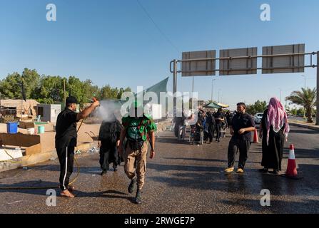 Najaf, Irak. September 2023. Ein Mann streut Wasser auf schiitische muslimische Pilger, die von Najaf in Richtung der Schreinerstadt Karbala marschieren. Jedes Jahr pilgern Millionen schiitische Muslime und einige aus anderen Glaubensrichtungen zu Fuß von verschiedenen Städten im Irak und Iran in die heilige Stadt Karbala. Diese Pilgerfahrt erinnert an Imam Hussein, den Enkel des Propheten Mohammed, der 680 n. Chr. in einer Schlacht starb. Am 40. Tag der Trauer um Hussein, bekannt als Arbaeen, kommen Pilger in Karbala zusammen, um an seinem Heiligtum Tribut zu zollen. Auf dem Weg stellen Freiwillige Nahrung, Wasser und Unterschlupf zur Verfügung Stockfoto