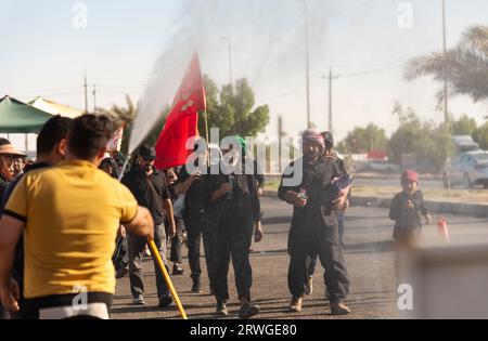 Najaf, Irak. September 2023. Ein Mann streut Wasser auf schiitische muslimische Pilger, die von Najaf in Richtung der Schreinerstadt Karbala marschieren. Jedes Jahr pilgern Millionen schiitische Muslime und einige aus anderen Glaubensrichtungen zu Fuß von verschiedenen Städten im Irak und Iran in die heilige Stadt Karbala. Diese Pilgerfahrt erinnert an Imam Hussein, den Enkel des Propheten Mohammed, der 680 n. Chr. in einer Schlacht starb. Am 40. Tag der Trauer um Hussein, bekannt als Arbaeen, kommen Pilger in Karbala zusammen, um an seinem Heiligtum Tribut zu zollen. Auf dem Weg stellen Freiwillige Nahrung, Wasser und Unterschlupf zur Verfügung Stockfoto