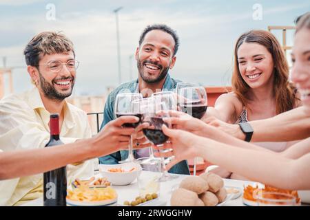 Gruppe von Freunden, die zusammen lächeln, reden und Weingläser auf einer Wochenend-Mittagsparty toasten. Verschiedene Freunde, die zu Hause essen und Spaß mit alkoholischen Getränken auf einer gesellschaftlichen Feier haben. Hochwertige Fotos Stockfoto
