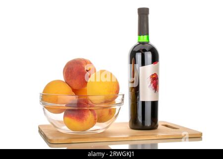 Eine Flasche Rotwein und einige reife Pfirsiche in einer Glasplatte auf einem Bambus-Küchenbrett, Makro, isoliert auf weißem Hintergrund. Stockfoto