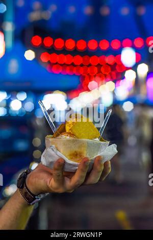 Hand hält Kokos- und Mangoeis in Kokosnussschale auf dem Jalan Alor Street Food Market in Kuala Lumpur Stockfoto