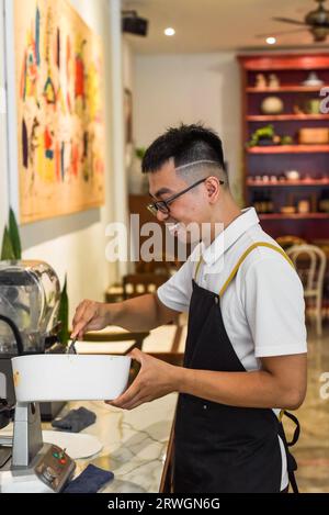 Vietnamesischer Küchenchef in einem einheitlichen Löffel und einer Schüssel mit flüssigem Teig für belgische Waffeln Stockfoto