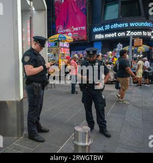 New York, USA - 24. Juli 2023: Zwei Polizisten aus New York überprüfen ihre Telefone auf dem überfüllten Times Square in Manhattan. Stockfoto