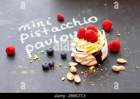 Nahaufnahme von Mini-Pistazien-pavlova-Kuchen mit frischen Himbeeren und Blaubeeren auf schwarzem Kreidebrett Stockfoto