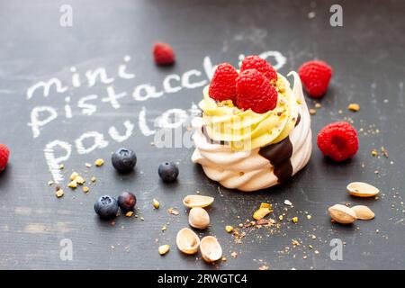 Nahaufnahme von Mini-Pistazien-pavlova-Kuchen mit frischen Himbeeren und Blaubeeren auf schwarzem Kreidebrett Stockfoto