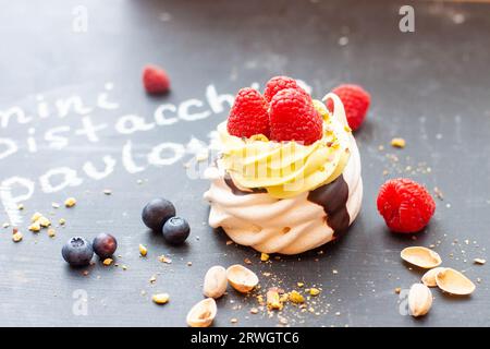 Nahaufnahme von Mini-Pistazien-pavlova-Kuchen mit frischen Himbeeren und Blaubeeren auf schwarzem Kreidebrett Stockfoto