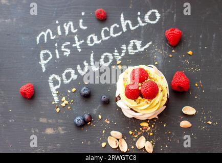 Nahaufnahme von Mini-Pistazien-pavlova-Kuchen mit frischen Himbeeren und Blaubeeren auf schwarzem Kreidebrett Stockfoto