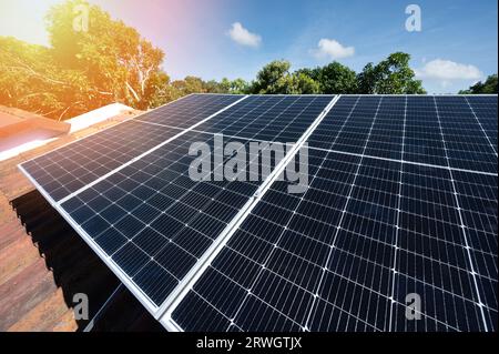 Thema "Ökostrom". Solaranlage auf dem Hausdach in blauem Himmel und grünem Baumhintergrund Stockfoto