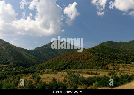 Bewaldete Hügel und blauer Himmel mit flauschigen weißen Wolken an einem sonnigen Septembertag im ländlichen Siebenbürgen. Stockfoto