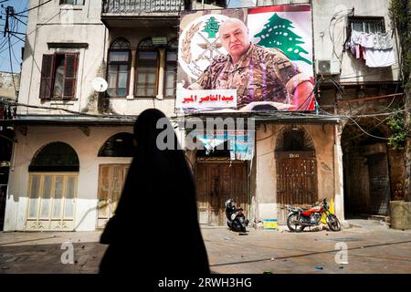 Verhüllte Frau in der Stadt Tripolis, Libanon. An der Wand des Hauses ist ein Wahlplakat eines Armeeführers. Stockfoto