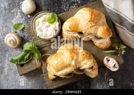 Französisches Gebäck, leckeres frisch gebackenes Sandwich. Veganes Essen. Croissant mit Frischkäse und Pilzen auf Steinhintergrund. Ansicht von oben. Stockfoto