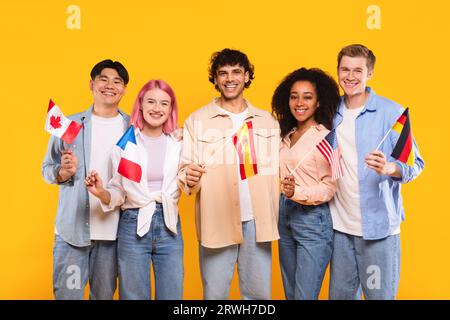 Glückliche multirassische Menschen, die verschiedene Länderflaggen halten und vor der Kamera lächeln, auf gelbem Hintergrund stehen Stockfoto