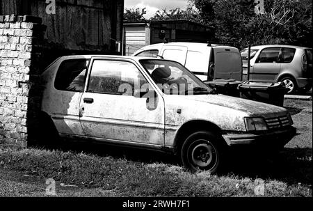 Es ist schon eine Weile da, was ein weißer Peugeot war, zerfällt langsam hinter einer Mauer, von wo er nicht aus Burscough, Lancashire, bewegt wird Stockfoto