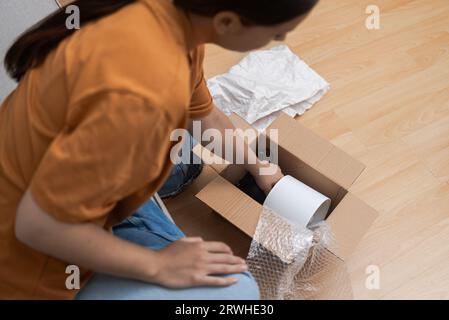 Frau wickelt ihr Paket mit Schreibtischleuchte aus, Wohndekoration entsteht aus der Lieferung im Online-Shop Stockfoto